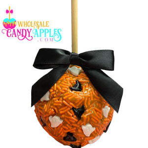 An orange candy apple with a black ribbon tied around it, decorated with orange and white sprinkles and black candy pieces.
