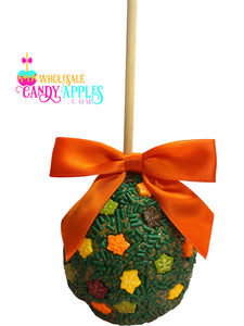 A candy apple with a green and orange color scheme, adorned with a red ribbon and sprinkled with various candy pieces.