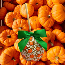 A candy apple with a green ribbon is surrounded by numerous orange pumpkins, creating a festive autumn scene.