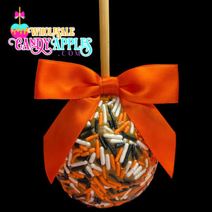 An orange candy apple with a red ribbon and sprinkles, displayed against a black background.