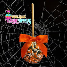 An orange candy apple with a red ribbon and sprinkles, displayed against a black background with a spider web pattern.