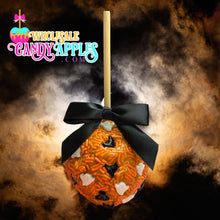 A candy apple with a black ribbon and orange and white candy pieces is displayed against a dark, cloudy background.