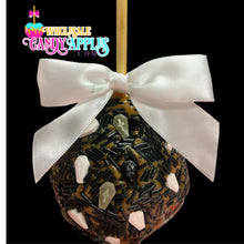 A candy apple with a white ribbon and black and white skull decorations, set against a black background.
