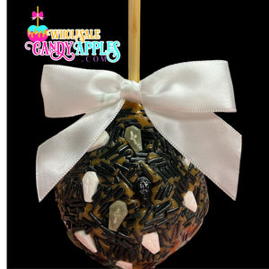 A candy apple with a white ribbon and black and white skull decorations, set against a black background.