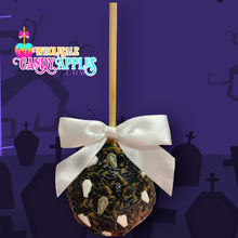 A candy apple with a white ribbon and black and white skull decorations, set against a purple background with silhouettes of gravestones.
