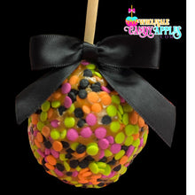 A candy apple with a black ribbon tied around it, decorated with colorful candy pieces in shades of orange, green, and black.