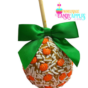 A candy apple with a green ribbon and orange and white sprinkles, featuring a pumpkin decoration.