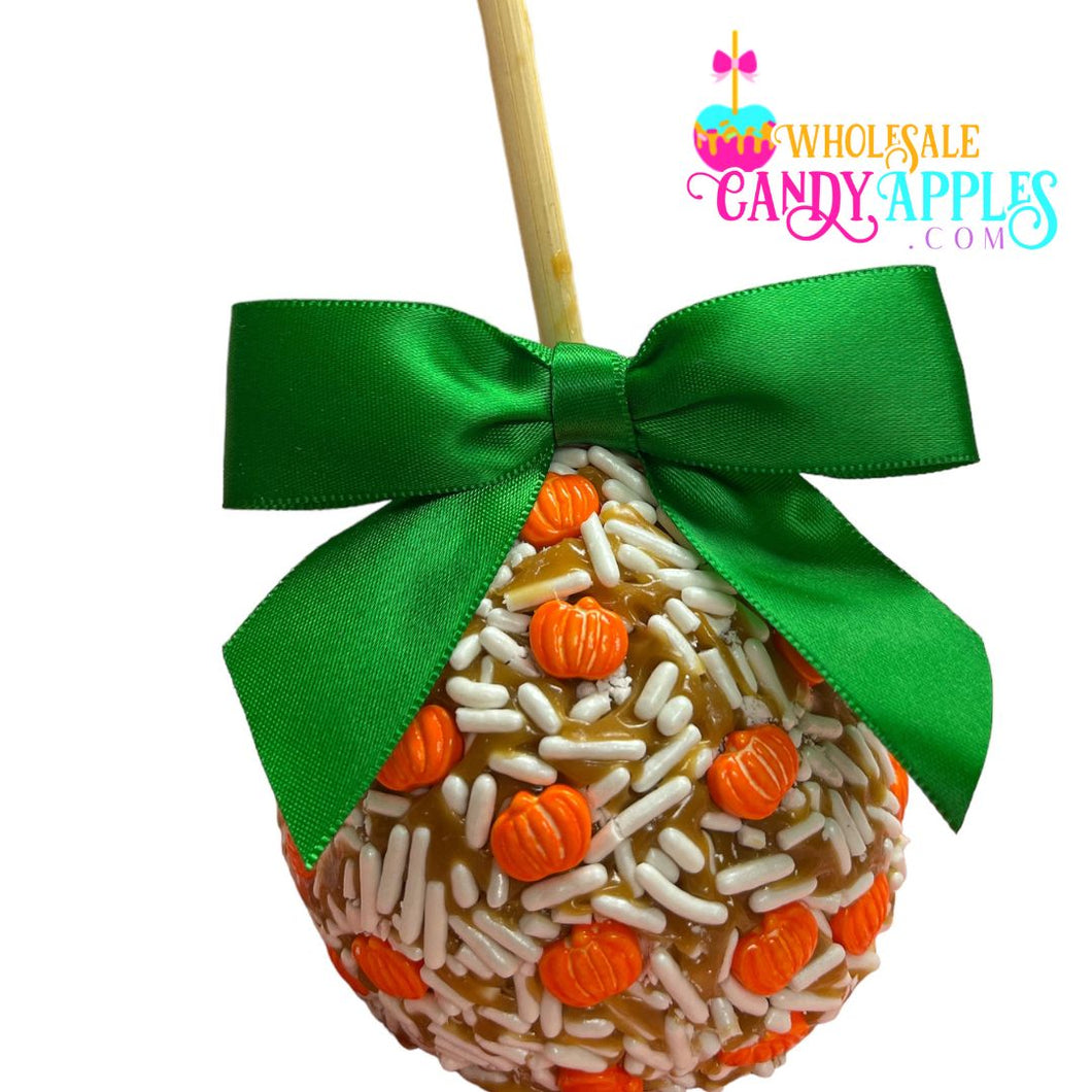 A candy apple with a green ribbon and orange and white sprinkles, featuring a pumpkin decoration.