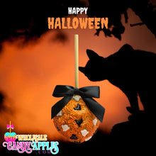 a Halloween-themed candy apple with a black ribbon, set against a dark orange and black background with a silhouette of a cat.